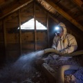 Weatherization technician blowing loose-fill cellulose insulation from an unfloored attic.