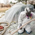 A technician is outside of a house injecting cellulose insulation into the exterior walls.
