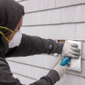 A weatherization installer fills an exterior wall cavity with blown cellulose insulation