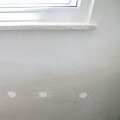 Four small round insulation access holes below a window are patched with a white one time spackle.