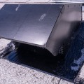 A black exhaust vent termination sealed into place on a gray asphalt shingled roof.