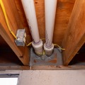 A gray mastic was applied around the edges of a basement rim joist cavity with white PVC piping between the joist cavity.
