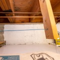 A partially white painted poured concrete foundation basement wall with uninsulated basement rim joist cavities above.