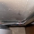A four inch metal duct connected to a dryer runs along the floor and up near the foundation wall of a basement.
