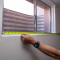 A weatherization installer measures the rough opening of a basement window using a tape measure.