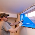 A weatherization installer peels the blue protective plastic from a newly installed interior storm window.