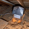 A reflective and insulated pre-fabricated cover placed over an attic light fixture was sealed to the attic celling with orange foam. 