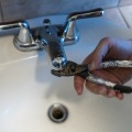 Close up of a person's hand holding a pliers over the outlet of a bathroom faucet. 