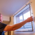 A person holds a basement storm window over the window opening of a home.