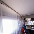 A weatherization installer holds a sheet of plastic while standing on a short ladder in a  residential home.