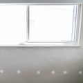 A series of two inch round holes patched with a white one-time spackle looking below a window of a residential home.