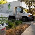 A weatherization services sign is posted in the yard of a home with a work truck in the background.