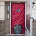 A blower door system with a red shroud is setup in the doorway of a residential home. 