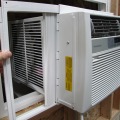 A hand holding an accordion panel of a window air conditioner.