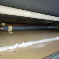 A light colored foam sealant along a wall with plumbing piping through the floor.