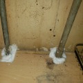 A white foam seal around two plumbing pipes as they pass through the subfloor of a home.