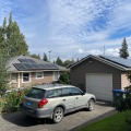 Dark gray and silver photovoltaic panels installed on a gray roof with no shading and lots of sun of a tan home. 