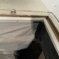 White weather stripping is fastened with silver screws on a tan wood interior of the access opening to a crawlspace. 