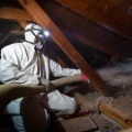 A weatherization technician is blowing a loose-fill cellulose insulation in an unfloored attic.