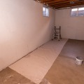 A white drop cloth placed over a section of a concrete basement flow with a short ladder placed in the corner. 