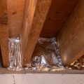 Foil faced insulation is cut to fit between two basement rim joist cavities, one cavity is sealed with gray mastic but not yet insulated.