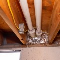 A foil faced insulation is installed in two of three basement rim joist cavities. The cavity in the middle has two white vent pipes in the cavity.
