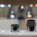 One old and one new faucet aerators sit on the edge of a bathroom sink.