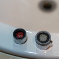 One old and one new faucet aerators sit on the edge of a bathroom sink.