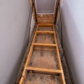 A pull-down attic stairway ladder is extended, looking up at a Styrofoam insulation panel.
