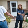 A weatherization installer holding a screw gun shakes hands with a client in front of her home. 