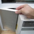 A hand holding a piece of rigid foam insulation to fill the opening of a window air conditioner unit.